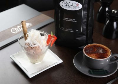 Featauring an gelato dessert. The dessert is served with candyfloss on top and a biscuit. Also in the photo is a cup of coffee with Carmen's restaurant menu in the back on the table