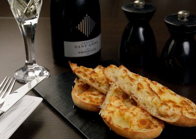 Cheesy bread on a black board and a bottle of wine in the background