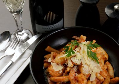 A pasta dish dished up on a big round black plate and o bottle of wine in the bacground